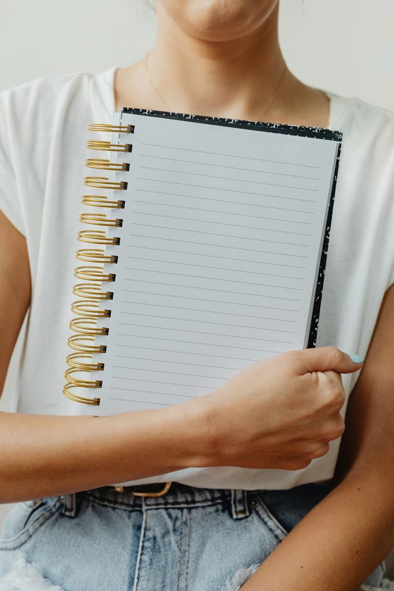 Close-up of a woman holding a blank spiral notebook, ideal for note-taking or creative journaling.