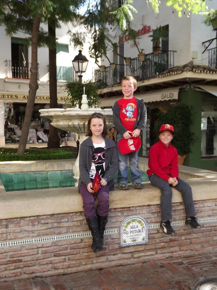 Trois enfants d'une famille nombreuse en voyage à la Costa del Sol en 2012, posant devant une fontaine en Espagne – L’Imparfaite Aventure