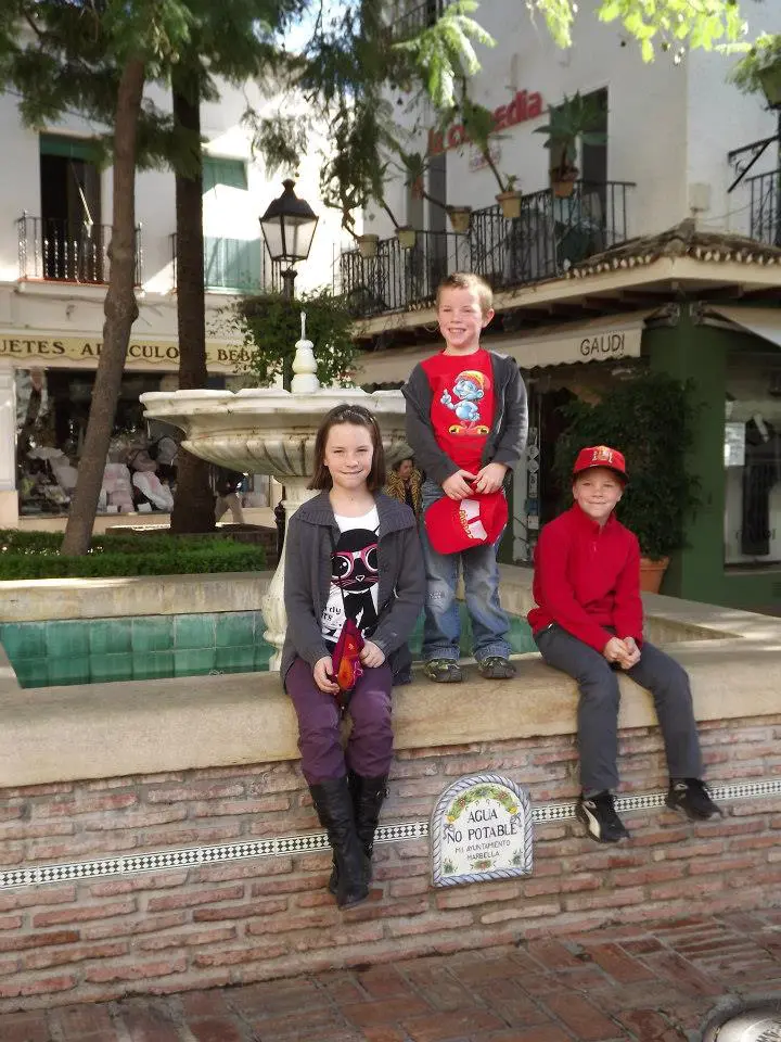 Trois enfants d'une famille nombreuse en voyage à la Costa del Sol en 2012, posant devant une fontaine en Espagne – L’Imparfaite Aventure